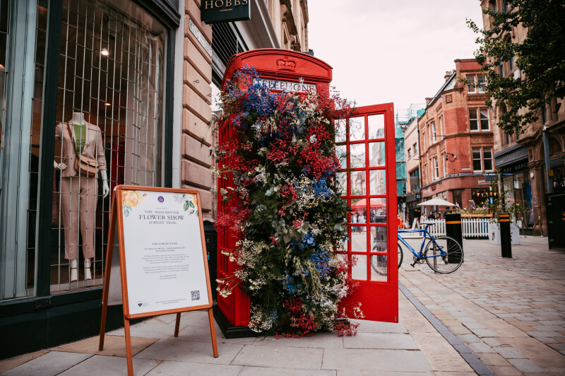 A red telephone box with its door open bursting with flowers.