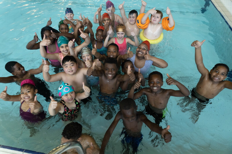 A groups of young people stood in a swimming pool giving a thumbs up.