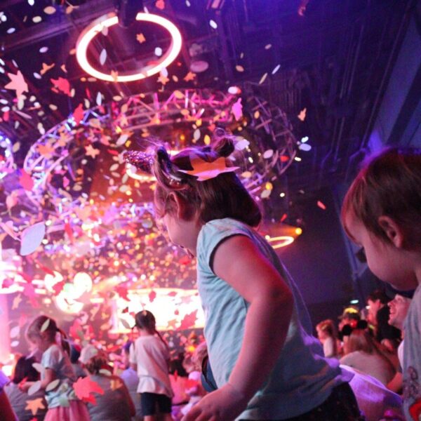 Children dancing as colourful confetti falls down onto them.