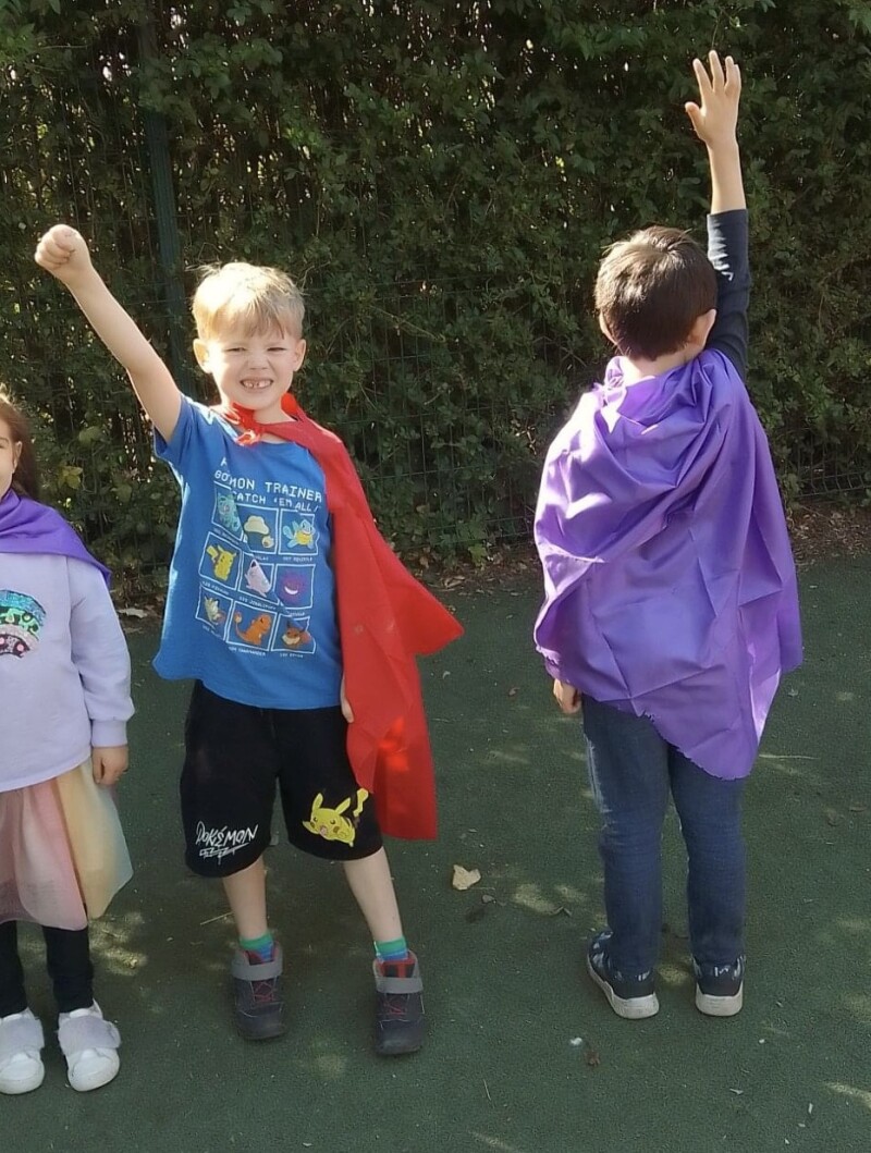 Two children wear capes and pretend to be super heroes.