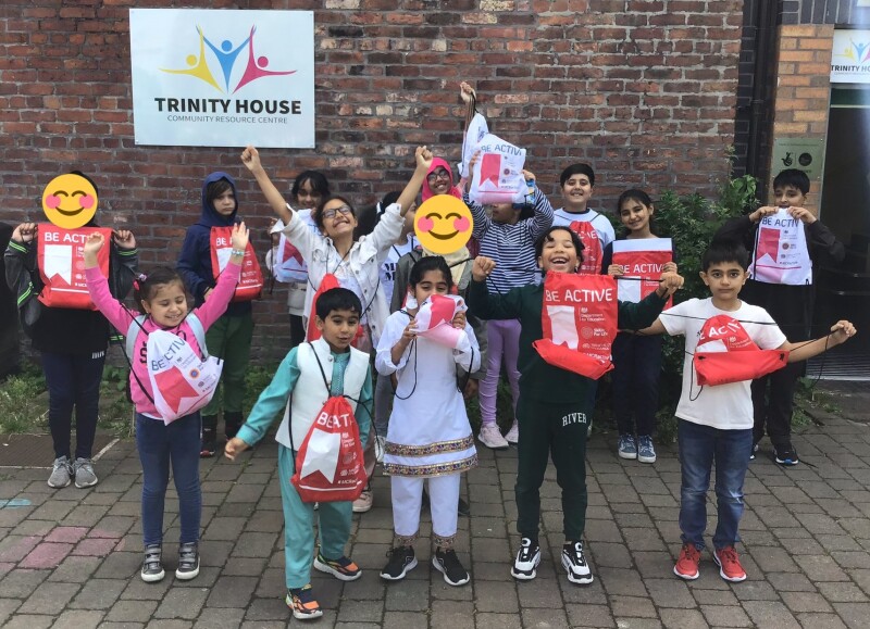 A group of happy children standing in front of a sign for Trinity House.