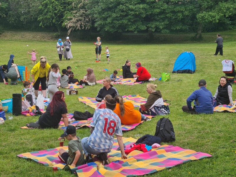A group of different families and people sat down on picnic blankets in a field.