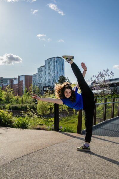 A female dancer does a high kick in Mayfield Park, Manchester