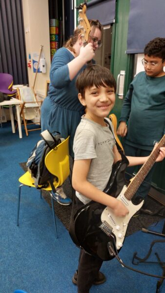 A young person smiling holding a guitar.