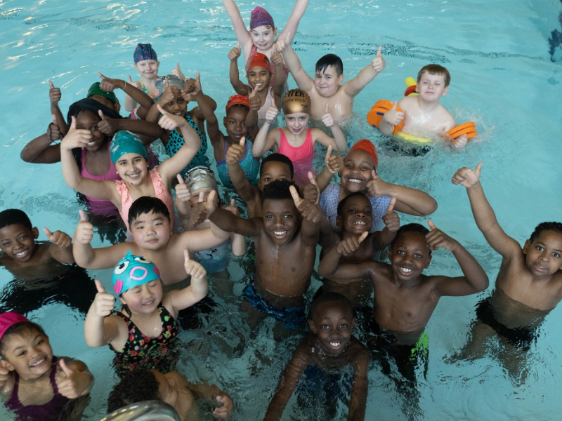 A group of young people stood in a swimming pool looking very happy.
