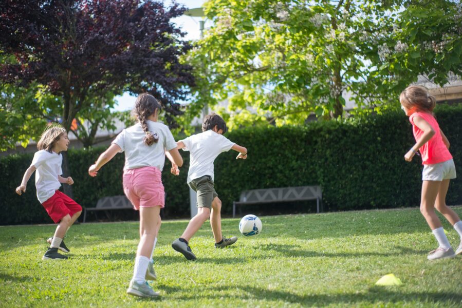 A groups of children playing football outside on grass.