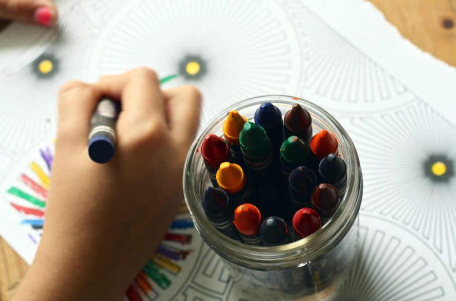 A pot of different coloured crayons as somebody draws on paper.