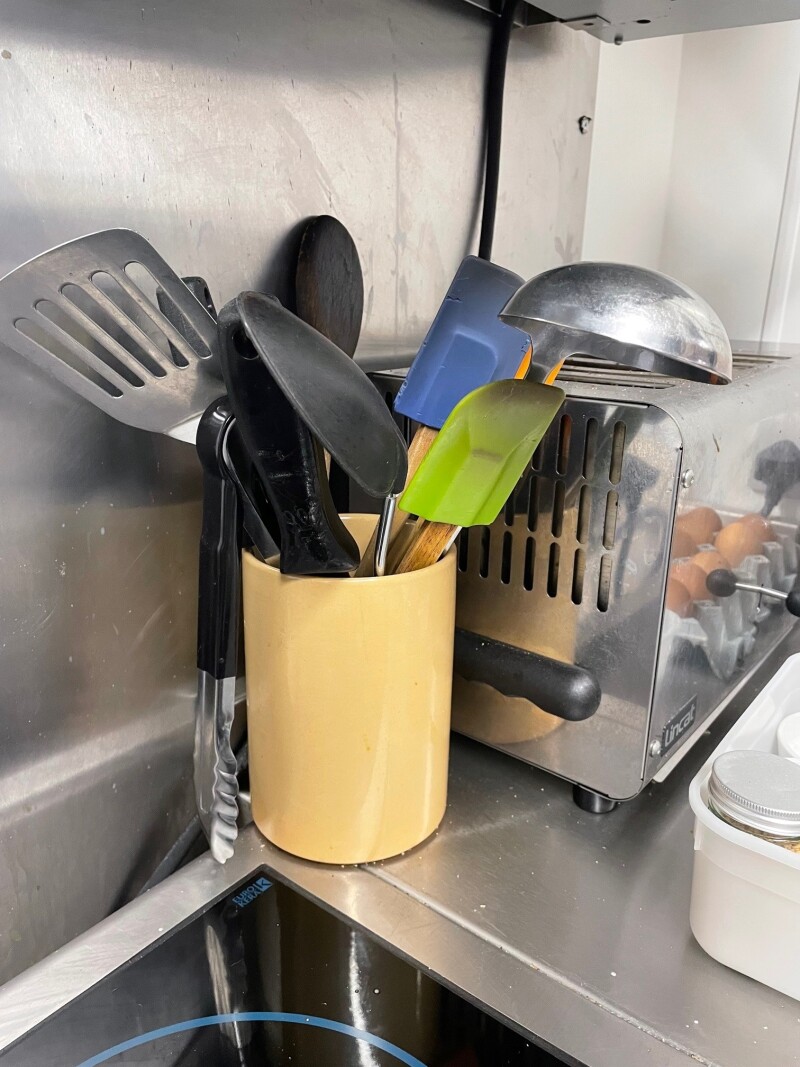A yellow pot filled with cooking utensils on a kitchen surface.