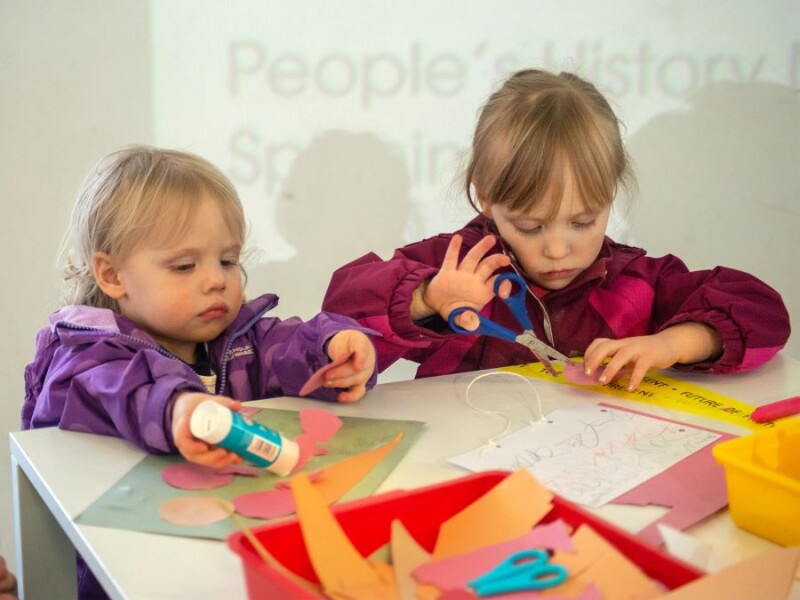 Two children using scissors, a glue stick and colourful papers.