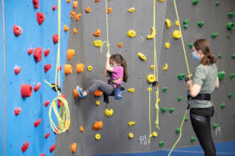 A young person climbing up a climbing wall wearing a safety harness.