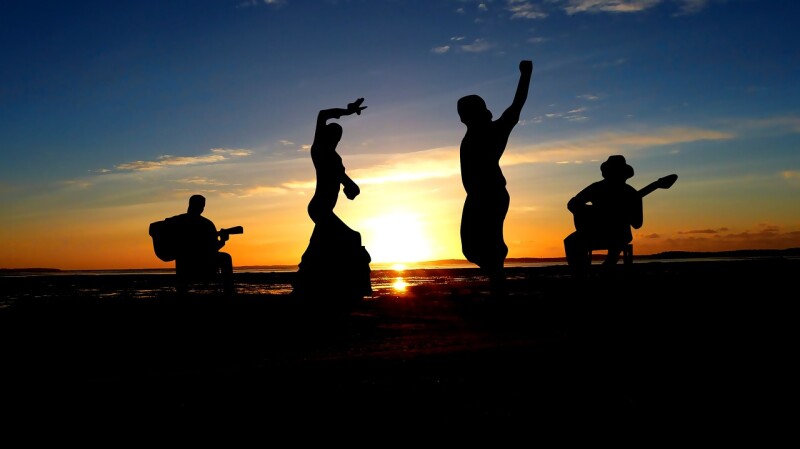Silhouettes of people dancing the flamenco against a sunset sky.