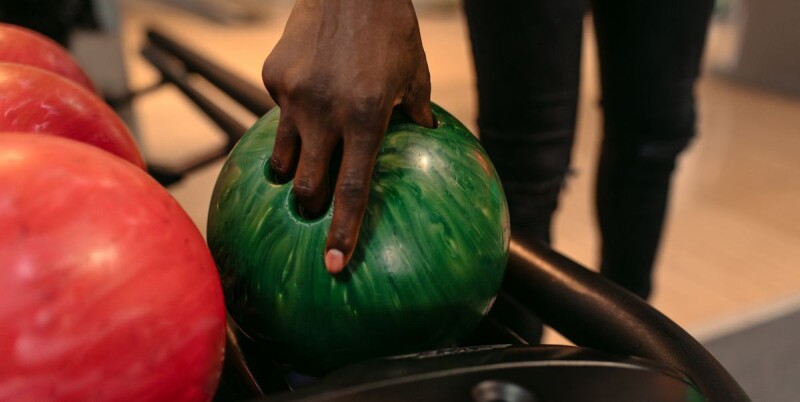 A hand reaches down to pick up a bowling bowl.