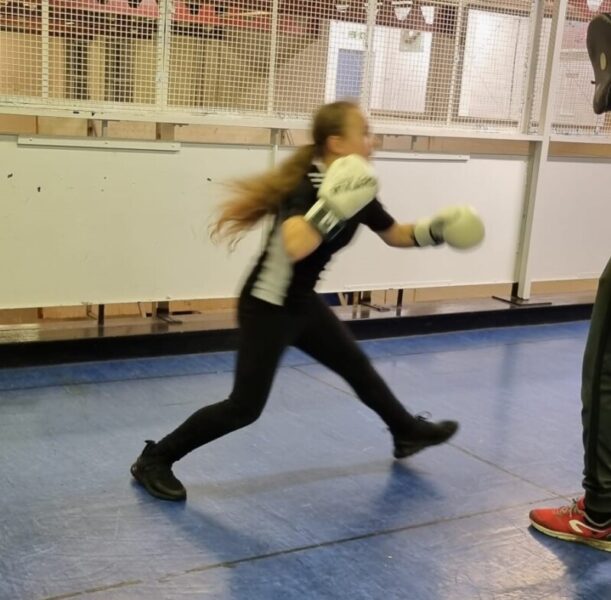 A young person spars wears boxing gloves.