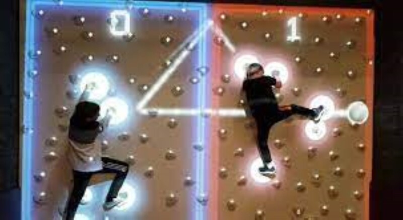 Two young people climbing up a climbing wall.