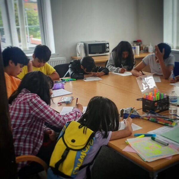 A groups of young people sitting around a table as they write.