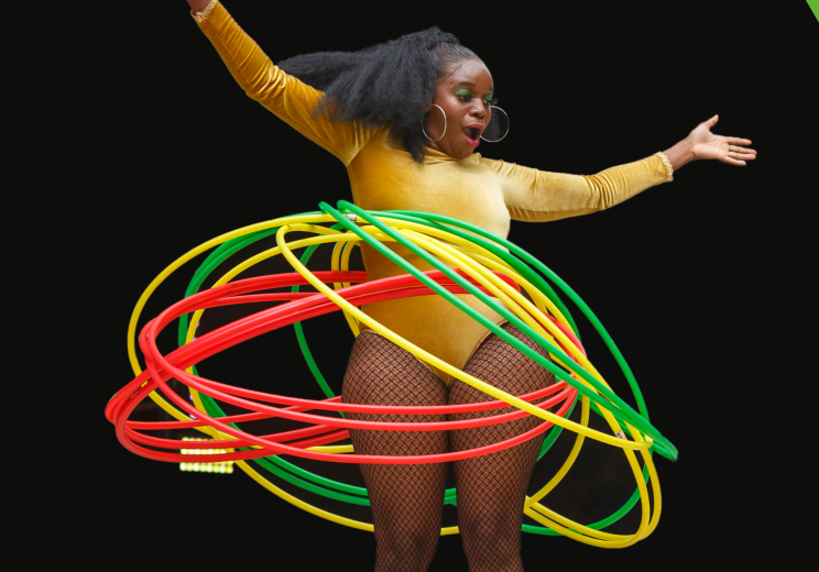 A person (Natasha Moonshine) is wearing spinning multiple hoops round them on a black background.