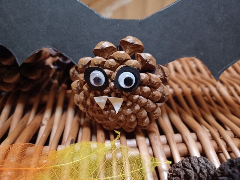 A model of a bat, with googly eyes and paper fangs, that has been crafted out of a pine cone.