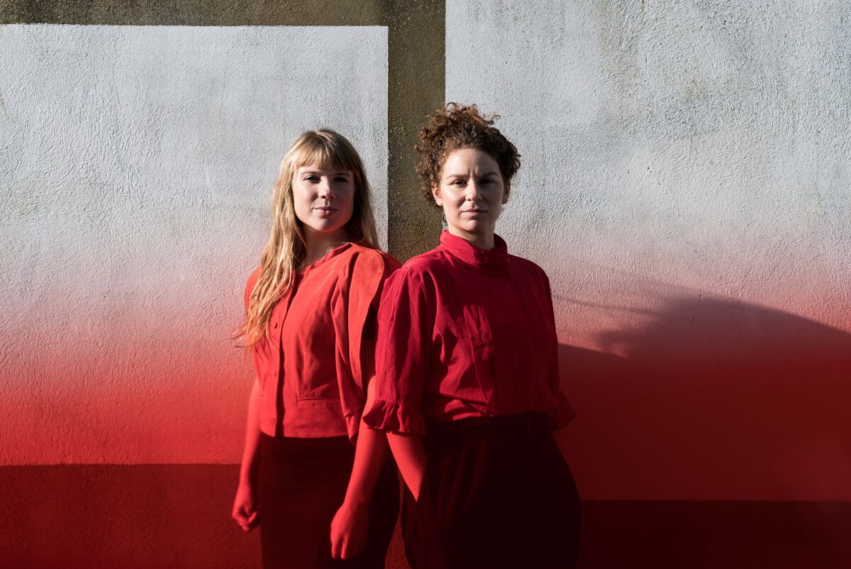The folk band Fran and Flora stand next to eachother wearing red shirts.