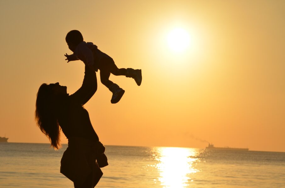 The silhouette of a mother holding her baby up in the air on a beach during sunrise.