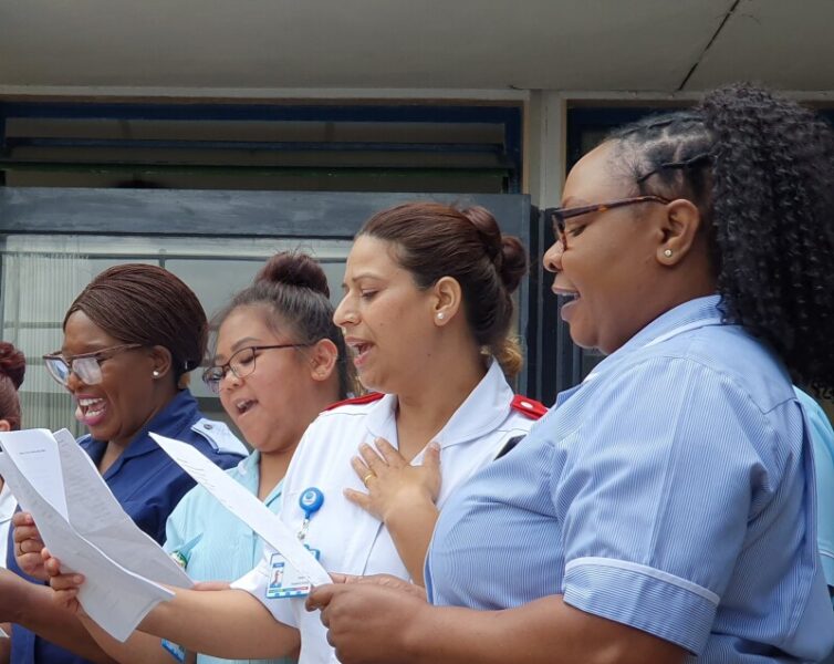 A group of NHS staff singing as a choir outdoors.