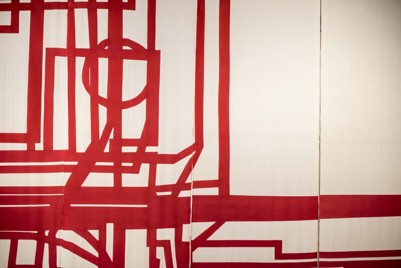 An artwork consisting of a series of red lines and shapes painted onto a white canvas.