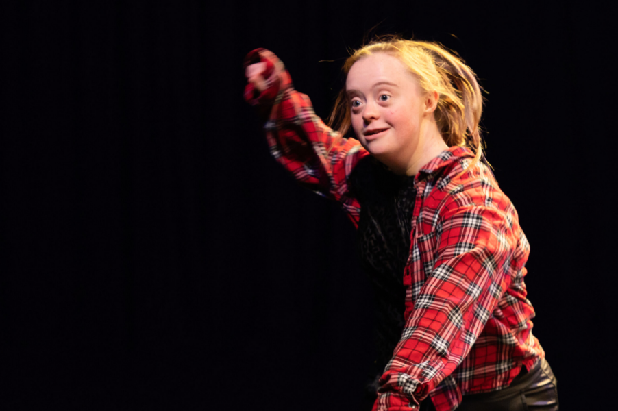 A young performer wearing a red checked shirt stands with one arm raised in the air.