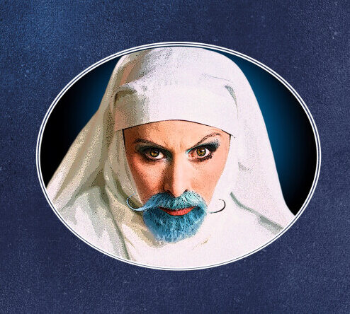 Head and shoulders of a person dressed in white clothes and a white headscarf with a short blue beard and moustache.