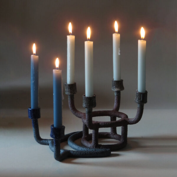A black ceramic candle holder with six lit candles.