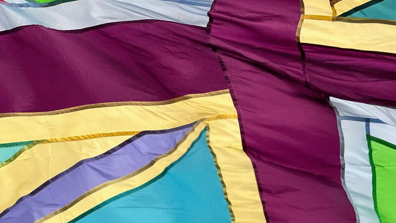 A close up of a union jack flag in plum, pale yellow, team and green.