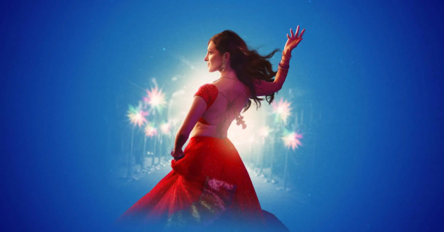 A beautiful female Indian dance stands wearing a red skirt and top with her right hand raised upwards. There are white sparkles around her on a blue background.