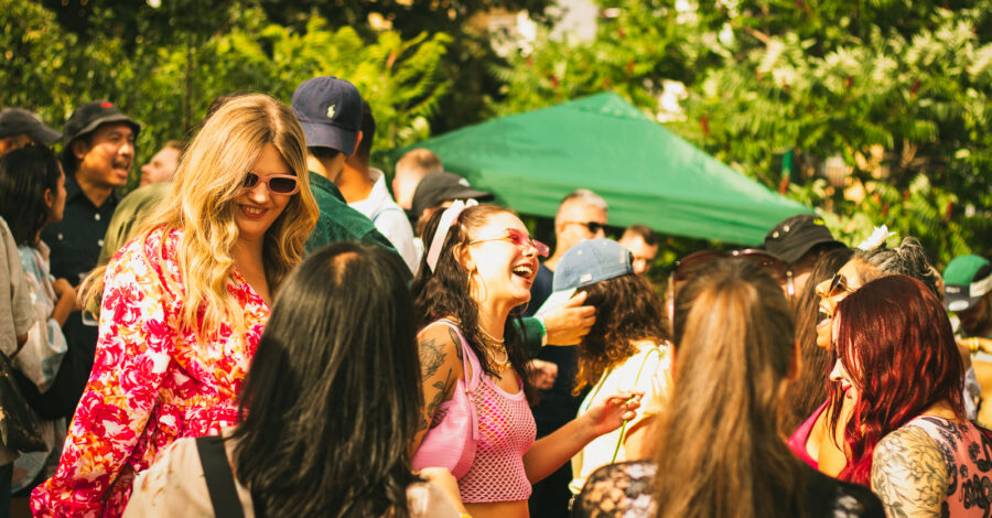 A group of festival goers enjoying themselves outside. The top of a green pergola is in the background.