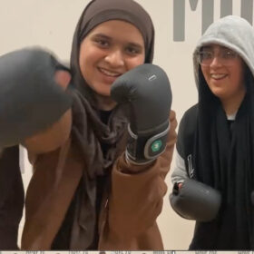 Two young girls wearing balck boxing gloves and smiling.