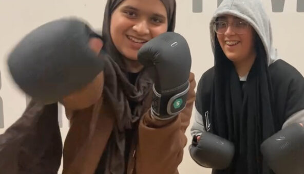 Two young girls wearing balck boxing gloves and smiling.