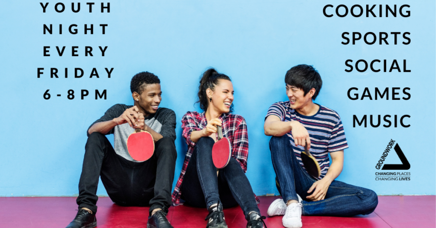 Three young people sit down on a red sports hall floor. They are holding red table tennis bats.