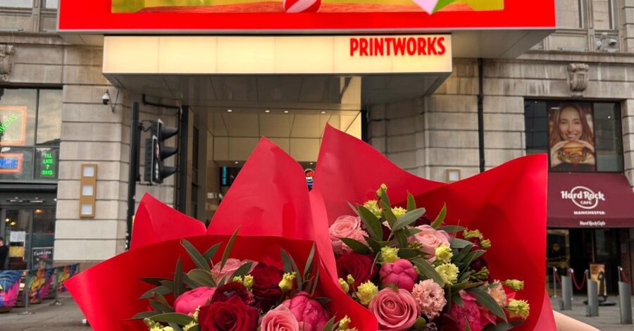 Two bouquets of red and pink flowers, wrapped in red paper held up in front of the Printworks entrance.
