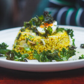 A white plate with a delicious looking dome of yellow rice, topped with half a boiled egg and some green salad leaves.