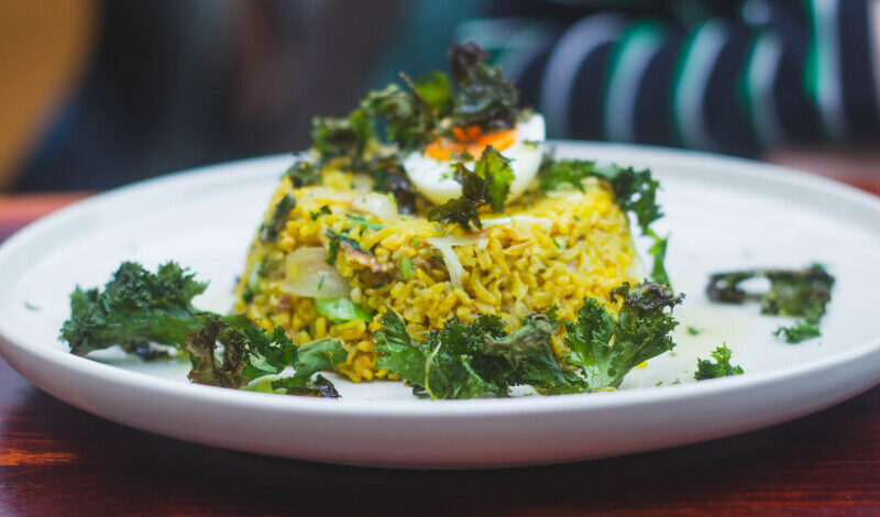 A white plate with a delicious looking dome of yellow rice, topped with half a boiled egg and some green salad leaves.