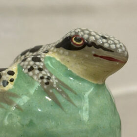 A ceramic frog painted with a green chest and a dotted white, grey and black head and limbs.