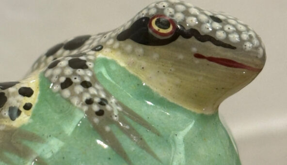 A ceramic frog painted with a green chest and a dotted white, grey and black head and limbs.
