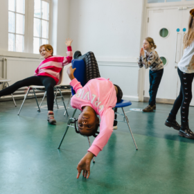 A group of young people posing on chairs in a drama class.