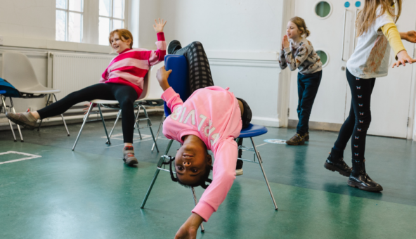 A group of young people posing on chairs in a drama class.