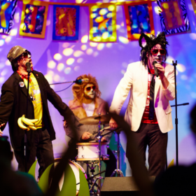 Three performers are dressed up in fancy dress on stage. One sings into a microphone.