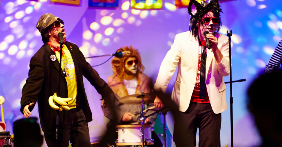 Three performers are dressed up in fancy dress on stage. One sings into a microphone.