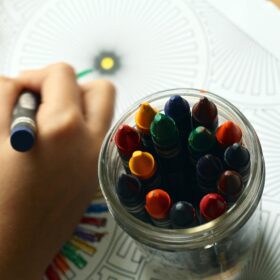 A glass jar of different coloured crayons and a child's hand drawing.