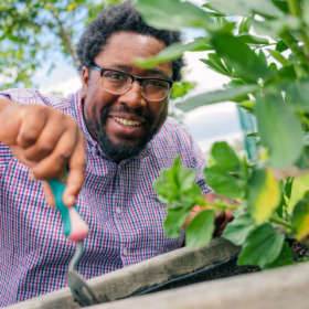 A man smiles as he digs a trowel into a planter.