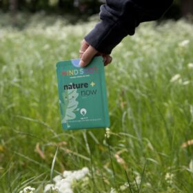 A person walking through long grass holding a green packet which reads "mind shot".
