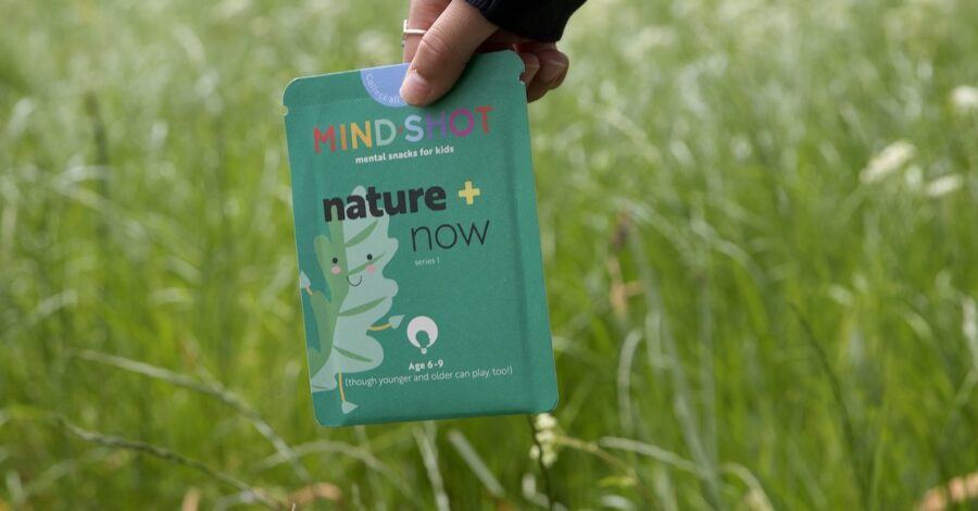 A person walking through long grass holding a green packet which reads "mind shot".