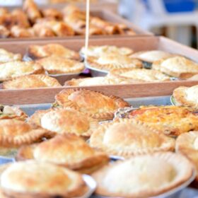 A selection of freshly baked pies in trays, displayed on a counter covered with blue table cloth.