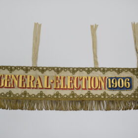 A banner with gold fringing, embroidery, and lettering reading: 'General Election 1906'.