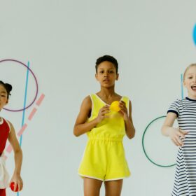 Three young people stand playing with brightly coloured balls and large rings.